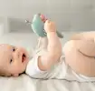 Baby ligt neer op laken met knuffel in de lucht