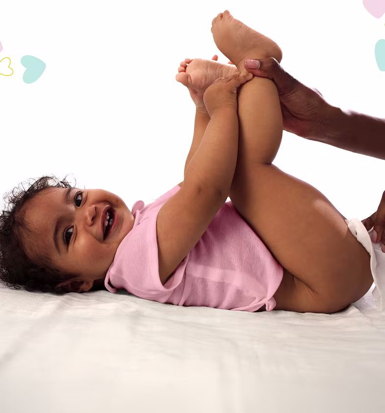 Um bebé está deitado de costas sobre uma superfície branca, levantando os pés enquanto um pai usa uma toalhita para limpar o rabo do bebé.