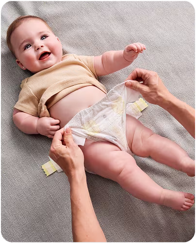 Un bebé alegre sonríe mientras su madre o padre le pone cuidadosamente un pañal limpio, asegurando comodidad y cuidado.
