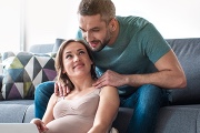 Expecting couple sitting on a couch, smiling and enjoying a cozy moment together at home.