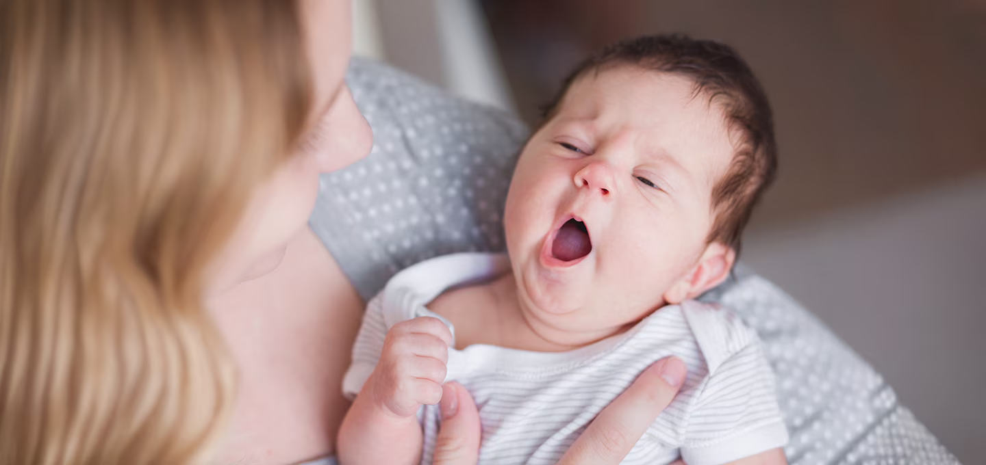 Baby yawning in mother's arms, wrapped in a cozy blanket.