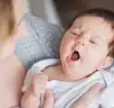 Baby yawning in mother's arms, wrapped in a cozy blanket.