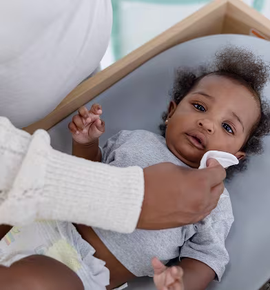 Imagen de una mamá limpiando la cara de su bebé durante un cambio de pañal Imagen de una mamá limpiando la cara de su bebé durante un cambio de pañal