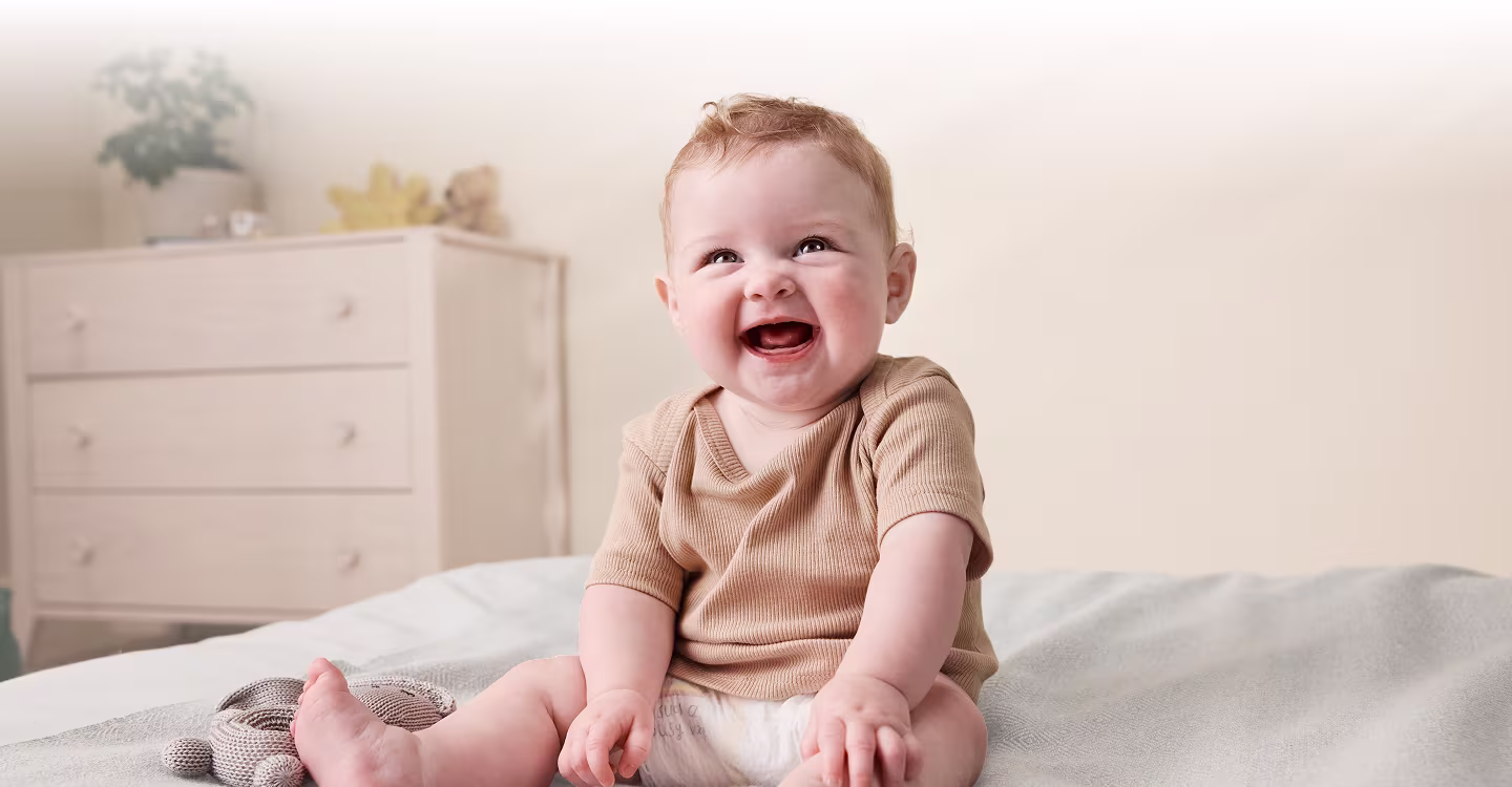 Uśmiechnięte dziecko na łóżku w pieluszce Pampers