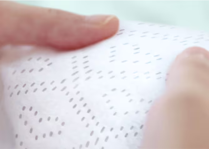 Nahaufnahme zweier Daumen, die das Innenvlies eine Pampers Premium Protection Windeln anfassen. Dank der Millionen von Mikroporen hält es Urin und flüssigen Stuhl von der Babyhaut fern.