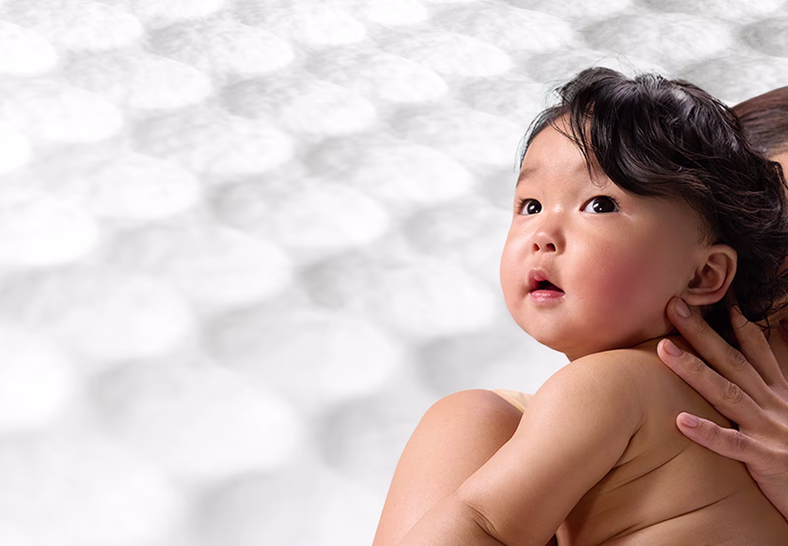 Eine Mutter hält ein Baby auf dem Arm, der Hintergrund zeigt die Waben-Struktur der Pampers® Aqua Soft Touch Feuchttücher