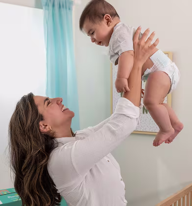 A loving parent lifting up their baby in a nursery wearing pampers baby dry