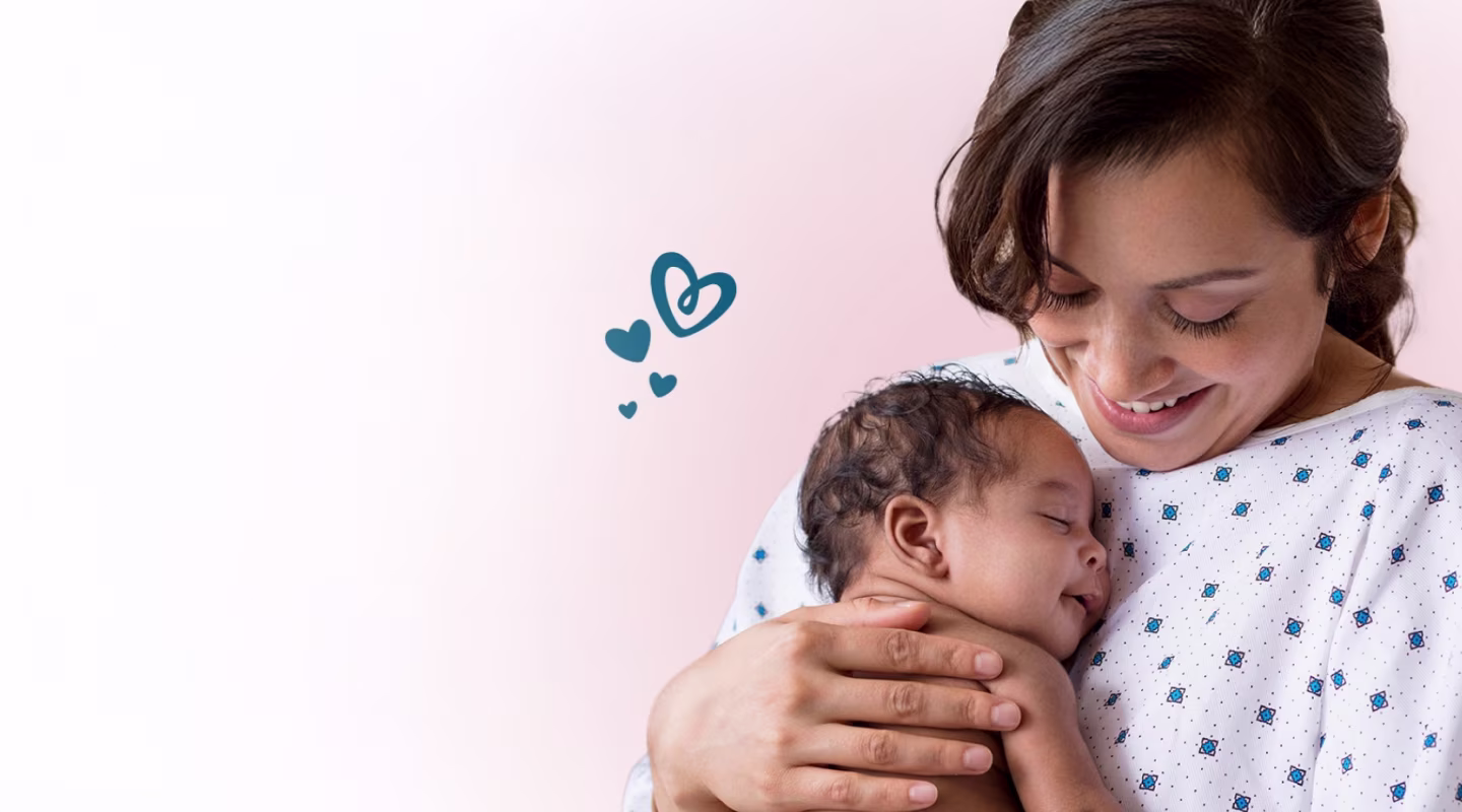 En leende mamma i sjukhuskläder håller en sovande nyfödd baby nära sitt bröst.