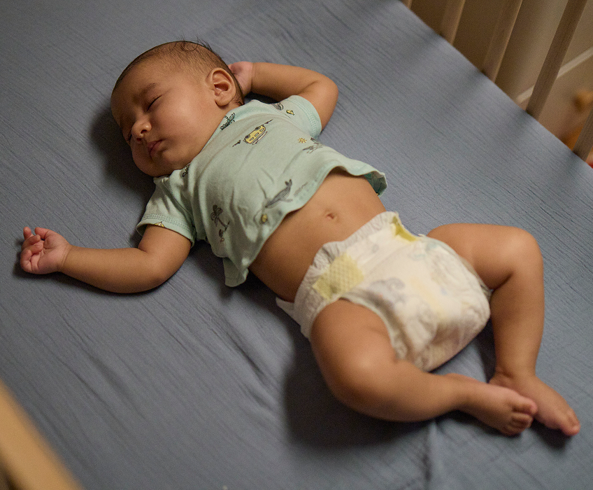 Baby wearing Pampers Swaddlers sleeping soundly on their dad’s chest