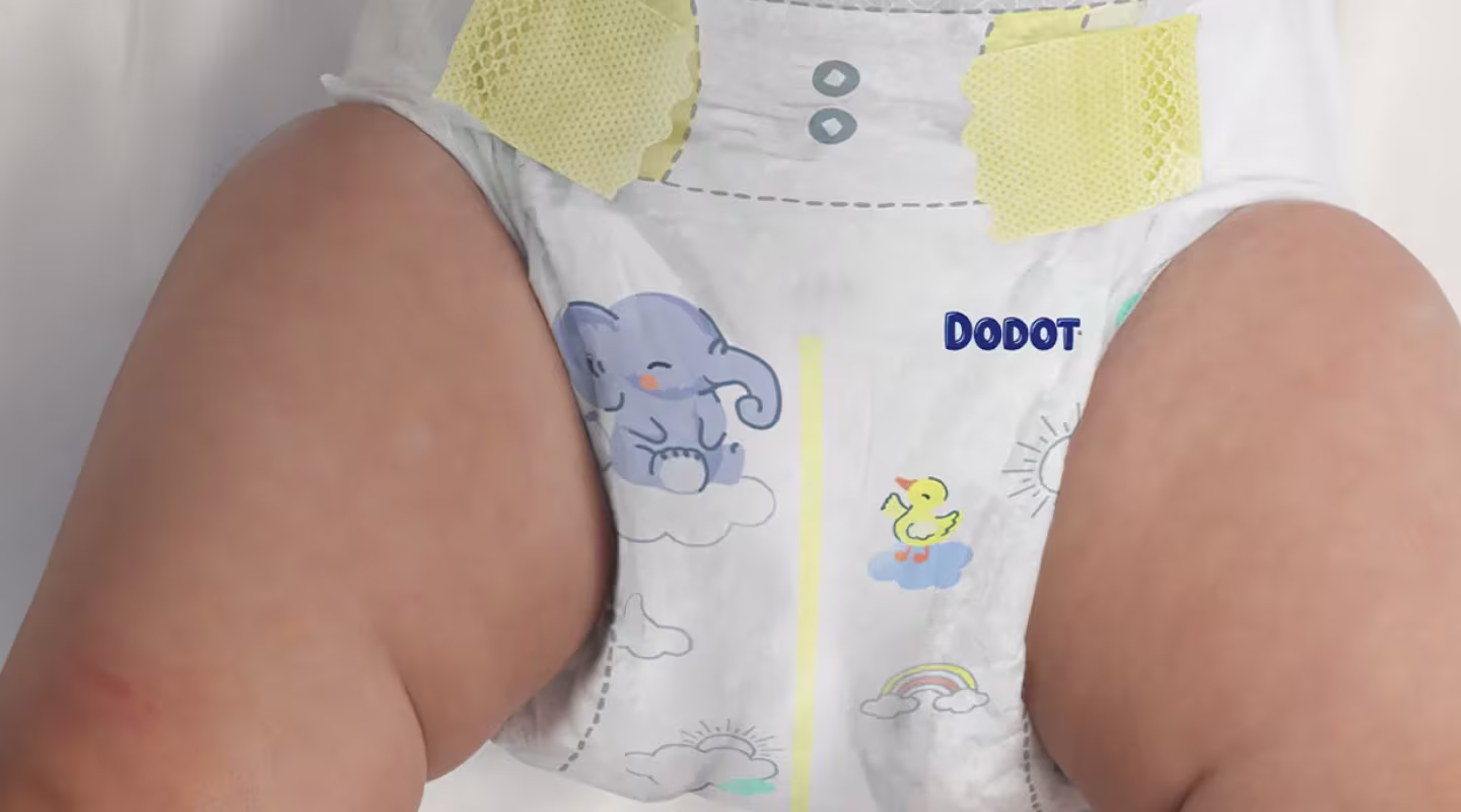 É mostrado um primeiro plano das pernas e da parte inferior do torso de um bebé enquanto usa uma fralda da marca Dodot e há um indicador de humidade.