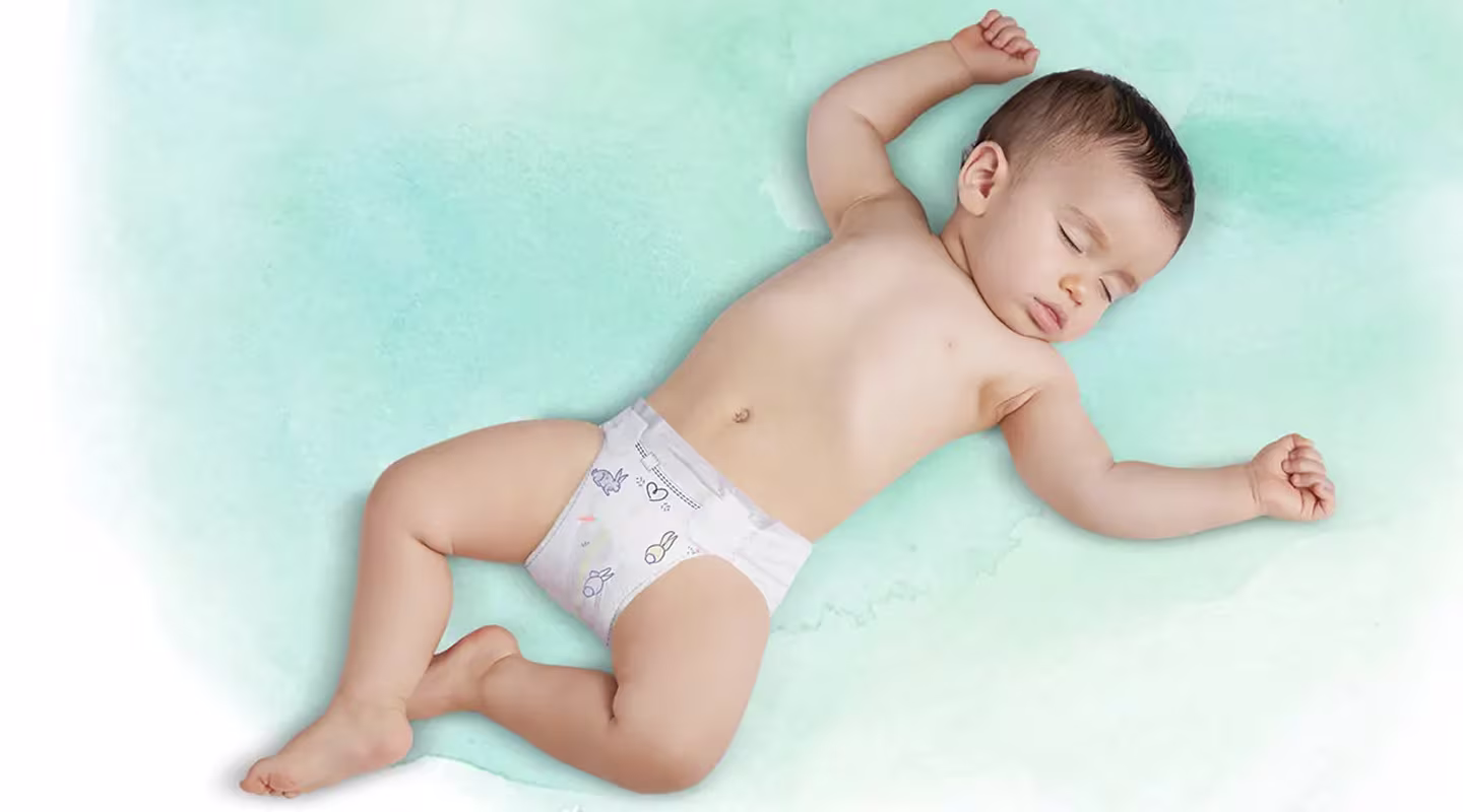 Selällään makaava nukkuva vauva, jolla on Pampers-vaippa päällään.