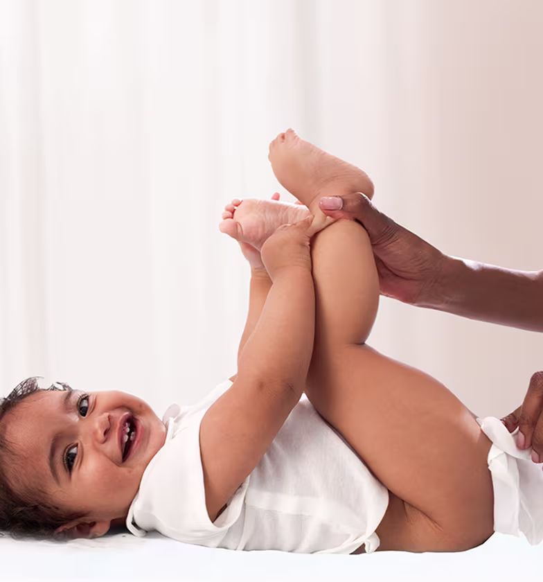 Um bebé está deitado de costas sobre uma superfície branca, levantando os pés enquanto um pai usa uma toalhita para limpar o rabo do bebé.