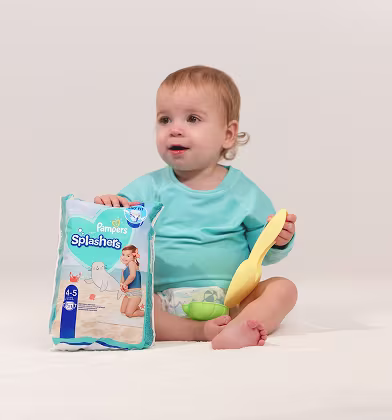 Un bebé feliz sostiene orgullosamente un paquete de Pampers Splashers, listo para un día divertido en la alberca con su pala. Un bebé feliz sostiene orgullosamente un paquete de Pampers Splashers, listo para un día divertido en la alberca con su pala.