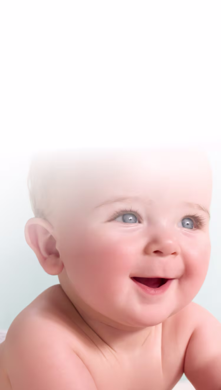 Een gelukkig baby’tje met blauwe ogen, liggend op zijn buik en glimlachend, terwijl het naar boven en opzij kijkt.