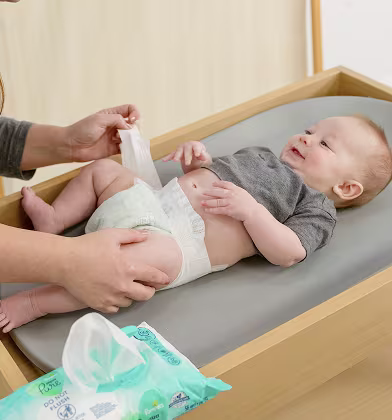 Mom changing her smiling baby’s diaper with a pack of aqua pure wipes sitting on the edge of the changing table Mom changing her smiling baby’s diaper with a pack of aqua pure wipes sitting on the edge of the changing table