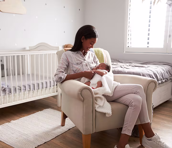Mother cradling baby in cozy nursery chair beside crib. Mother cradling baby in cozy nursery chair beside crib.