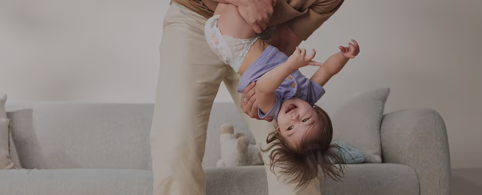A shot of a dad playing with their toddler. Both are smiling and laughing