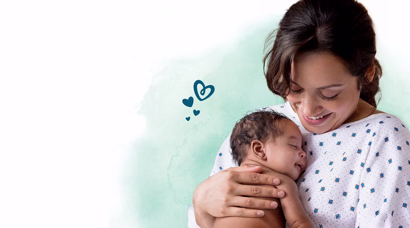 En leende mamma i sjukhuskläder håller en sovande nyfödd baby nära sitt bröst.