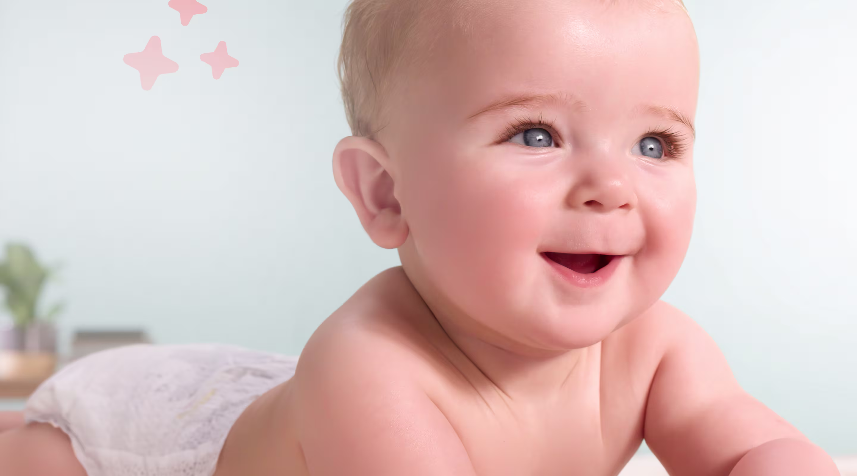 Een vrolijke baby met blauwe ogen, liggend op zijn buik en glimlachend, terwijl hij omhoog en opzij kijkt.