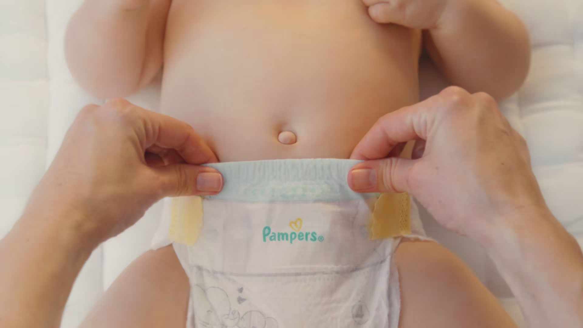 Un prim-plan arată două mâini care întind ușor scutecul Pampers Premium Care.