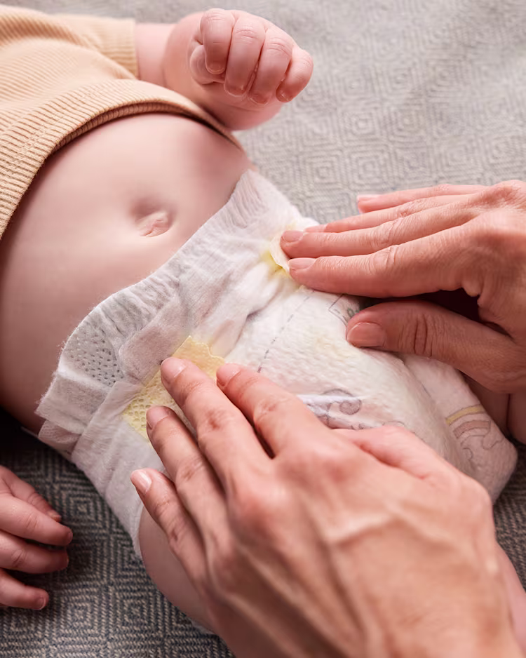 Elternteil, der sanft eine frische Windel mit den Klebestreifen sichert und dabei für Komfort und Pflege sorgt.