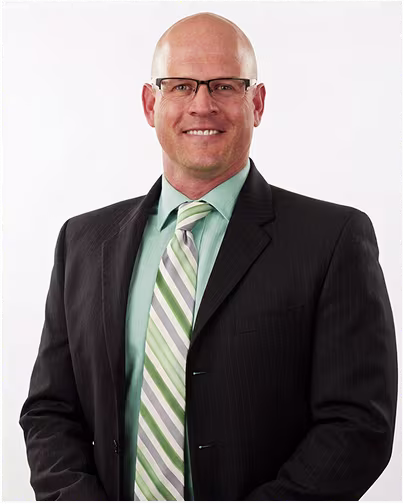 A bald male scientist with glasses, wearing a suit and striped tie, smiles.