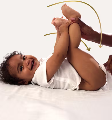 Un bebé está tumbado de espaldas sobre una superficie blanca, levantando los pies mientras un padre utiliza una toallita para limpiar el trasero del bebé.