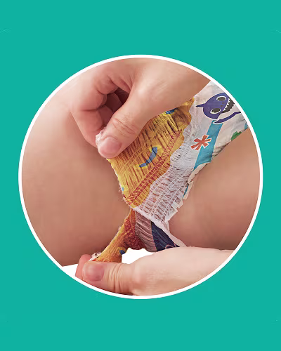 A close-up shot shows a parent’s hands tearing the side of a Baby Shark-themed swim diaper on a baby, highlighting the "Super easy-tear sides" feature.