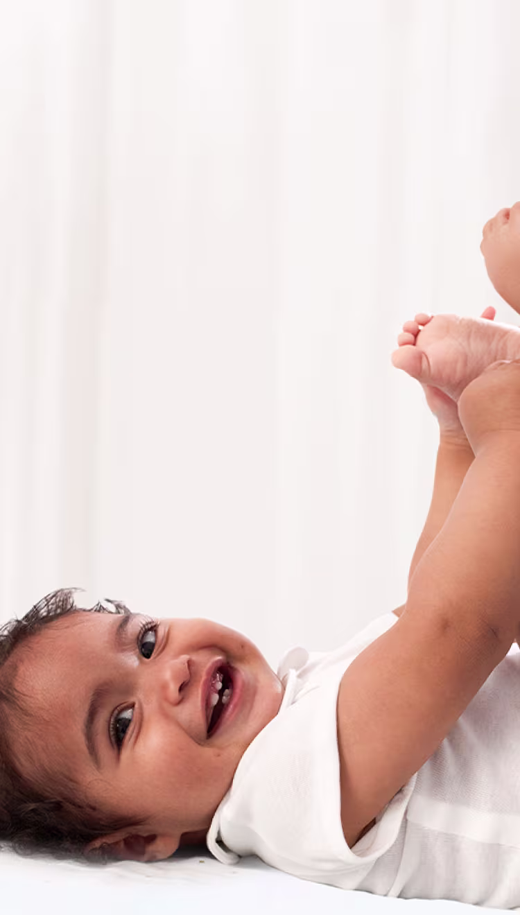 Um bebé está deitado de costas sobre uma superfície branca, levantando os pés enquanto um pai usa uma toalhita para limpar o rabo do bebé.