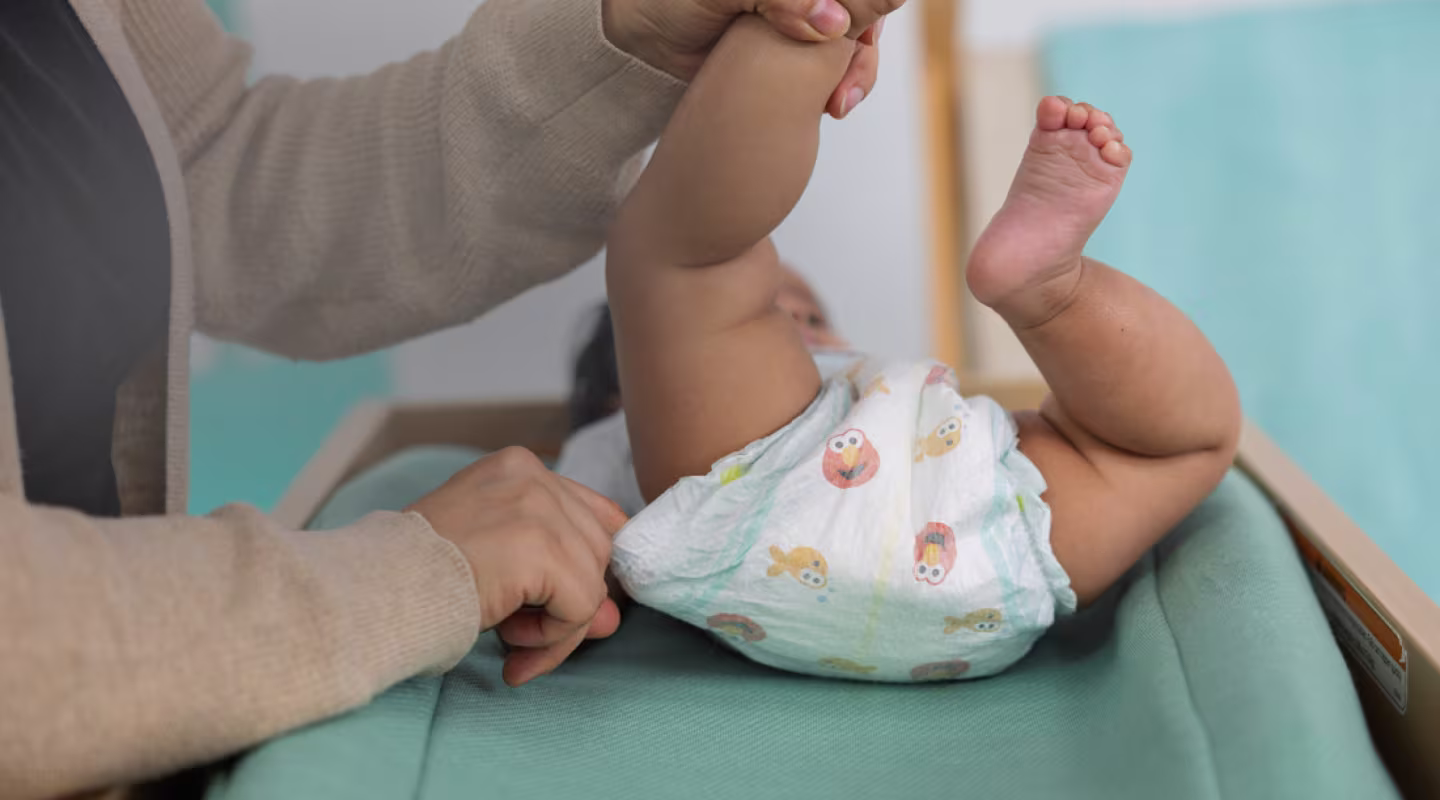 Un padre cariñoso revisa con delicadeza que el pañal quede bien ajustado alrededor de la pierna de su bebé, asegurándose de que esté cómodo y evitando fugas.