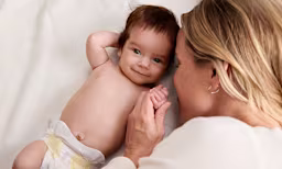Maman jouant avec son bébé souriant portant une couche Pampers, mettant en avant la sécurité.]