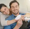 Smiling couple holding baby shoes on a couch.