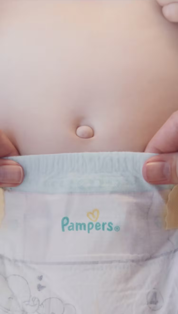 Een close-up toont twee handen die voorzichtig de buikriem van een Pampers-luier trekken, waardoor de flexibele en beschermende buikriem wordt gedemonstreerd.