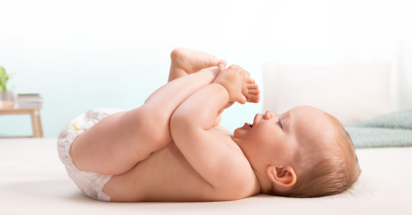 A baby lies on his back and playfully grabs his feet.