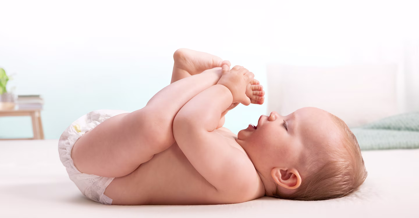 A baby lies on his back and playfully grabs his feet.
