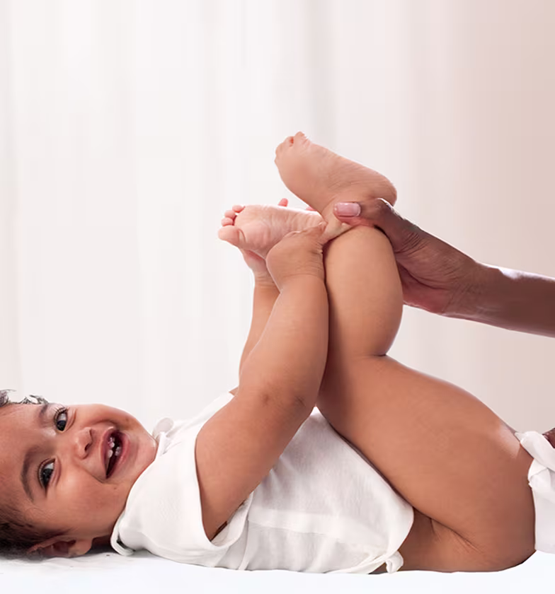 Un bebé está tumbado de espaldas sobre una superficie blanca, levantando los pies mientras un padre utiliza una toallita para limpiar el trasero del bebé.