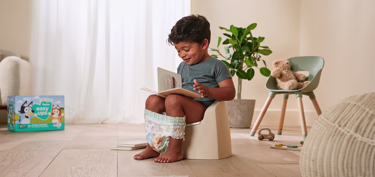 A toddler sitting on a potty, looking at a book