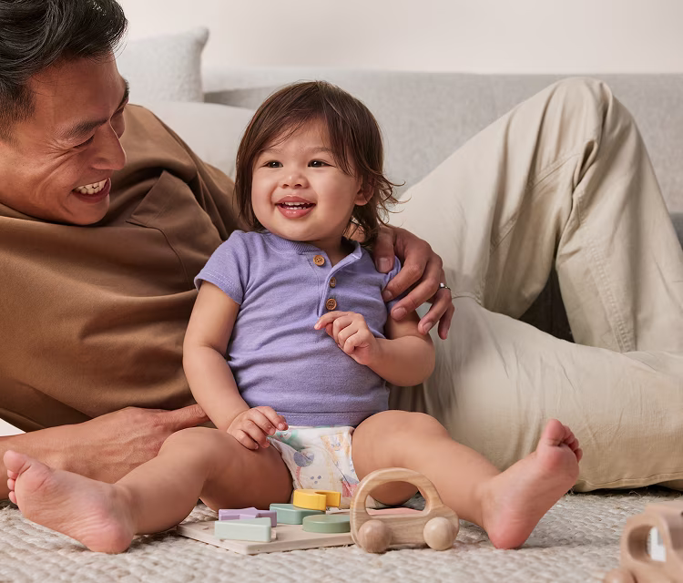 Baby sitting on floor next do their dad, playing with toys