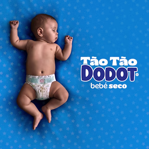 Um bebé com uma fralda Dodot dorme de costas sobre uma manta verde-azulada.