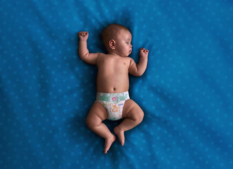 Um bebé que usa uma fralda Dodot dorme de costas sobre uma manta azul-esverdeada.