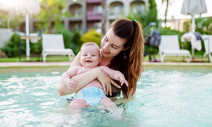 Una madre sostiene a un bebé en una piscina, el bebé lleva un pañal de agua.