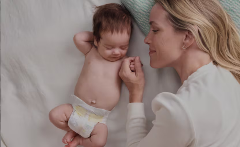 Äiti makaa vauvan kanssa, jolla on Pampers-vaippa päällään.