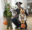 Family in cute animal and pirate costumes with pumpkin buckets, smiling indoors.