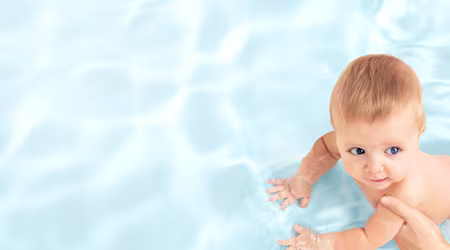 En baby ligger på rygg medan en person torkar babyns rumpa med en våtservett.