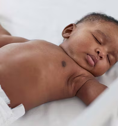 Un bébé dort sur le dos et porte une couche Pampers.