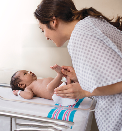 Una nueva mamá está cambiando el pañal de su recién nacido y limpiando el trasero del bebé con una toallita en una habitación del hospital.