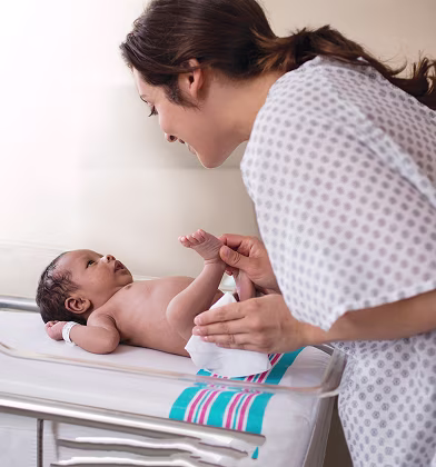 Una nueva mamá está cambiando el pañal de su recién nacido y limpiando el trasero del bebé con una toallita en una habitación del hospital.
