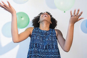 Person joyfully playing with balloons, wearing a blue patterned dress.