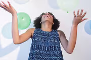 Person joyfully playing with balloons, wearing a blue patterned dress.