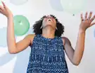 Person joyfully playing with balloons, wearing a blue patterned dress.